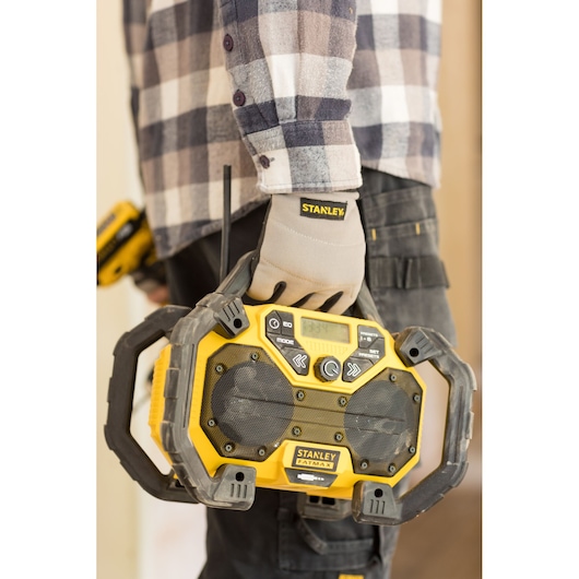 Stanley FMCR001B jobsite radio with rugged design, yellow and black, held by worker wearing gloves.