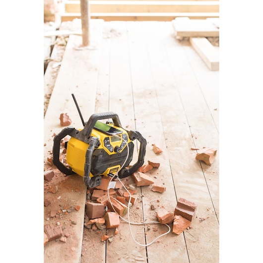 STANLEY FMCR001B jobsite radio on wood floor with debris and bricks, front angle.