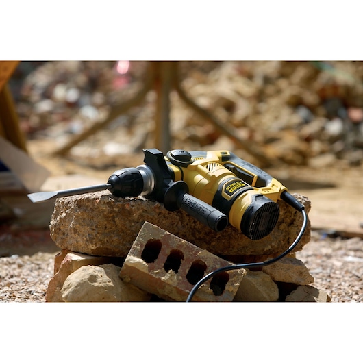 STANLEY FME1250K rotary hammer drill with chisel bit on construction debris, shown in outdoor setting.