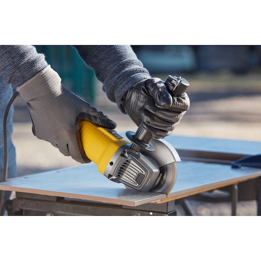 STANLEY FMEG220K angle grinder cutting tile, close-up of hands in gloves outdoors.