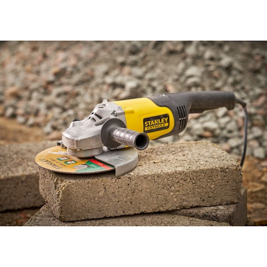 STANLEY FMEG232 angle grinder with yellow and black body, shown on concrete blocks, side view.