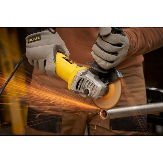 STANLEY FMEG615 angle grinder cutting metal pipe with sparks, close-up action shot.