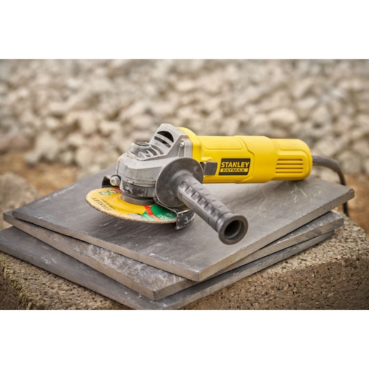 STANLEY FMEG615 yellow angle grinder on stacked tiles, side view.