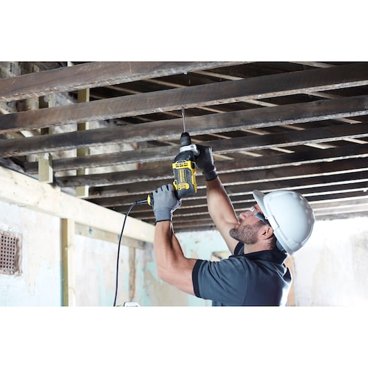 STANLEY FMEH750 corded drill being used overhead by worker with gloves and helmet in construction setting.