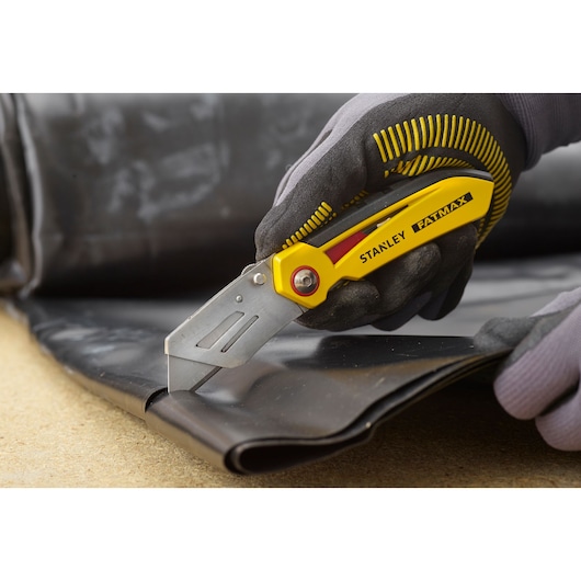 Stanley FMHT0-10827 utility knife cutting black material, close-up view, yellow and silver design.