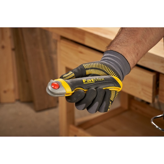 STANLEY FMHT0-20559 FatMax utility knife held in gloved hand, yellow and black handle, workshop background.