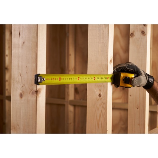 STANLEY FMHT0-33868 tape measure being used to measure wooden studs, close-up, construction setting.