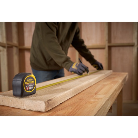 STANLEY FMHT0-33868 FATMAX tape measure on wooden beam in workshop, person marking measurements.