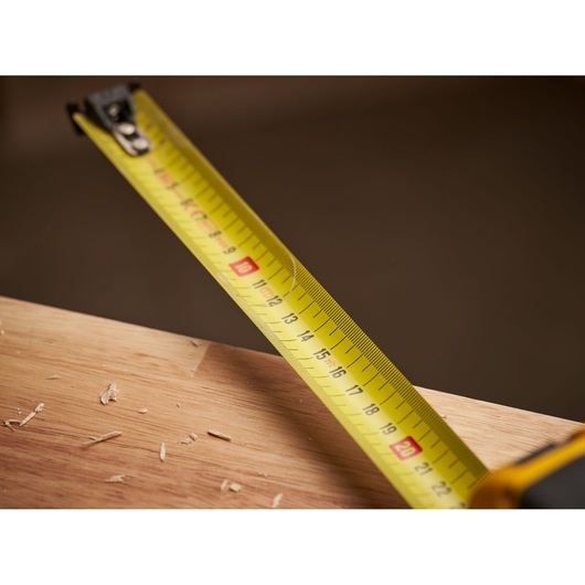 STANLEY FMHT0-33868 tape measure in use, yellow blade extended over wooden surface with wood shavings, close-up.