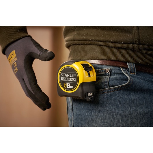 STANLEY FMHT0-33868 FATMAX magnetic tape measure clipped to jeans, worker in gloves nearby.