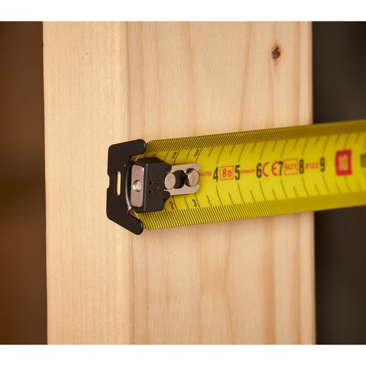 STANLEY FMHT0-33868 tape measure with yellow blade measuring wooden plank, close-up side view.