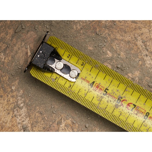 STANLEY FMHT0-33868 yellow tape measure close-up on dusty surface, showing centimeter markings.