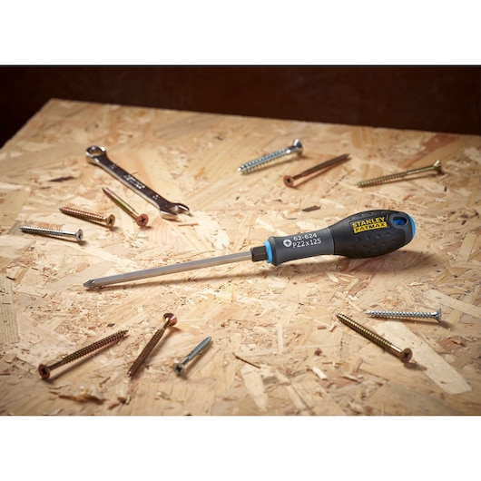 A STANLEY FATMAX screwdriver with a black and yellow handle is laying on a wooden surface, surrounded by several screws and a metal wrench.