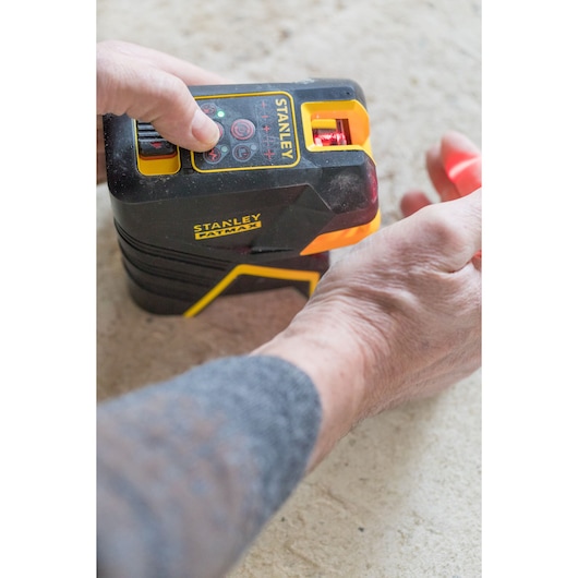 Photo of STANLEY FMHT1-77415 laser level tool in use, close-up of hands operating the black and yellow device.