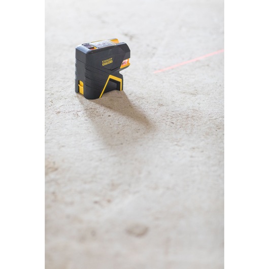 STANLEY FMHT1-77415 laser level on concrete floor projecting red horizontal line, product side angle.