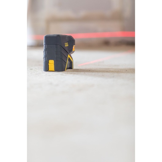 Stanley FMHT1-77415 cross line laser level on floor, side angle, projecting bright red laser lines.