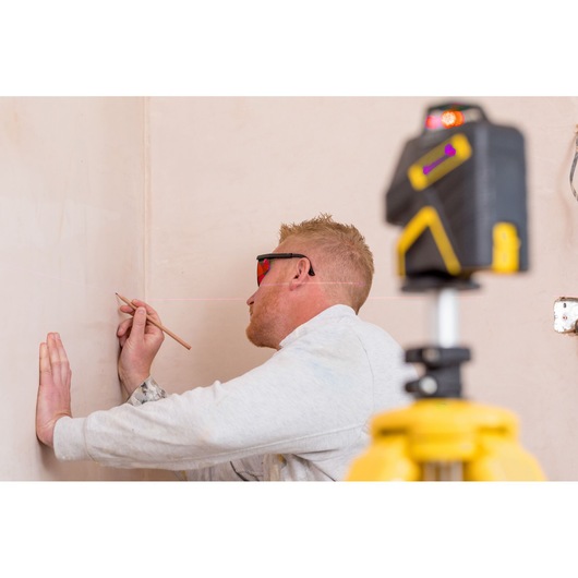 Photo of STANLEY FMHT1-77416 laser level on tripod projecting line while person marks wall.