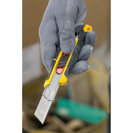 Photo of STANLEY FMHT10338-0 utility knife with yellow and black handle held in a gloved hand.