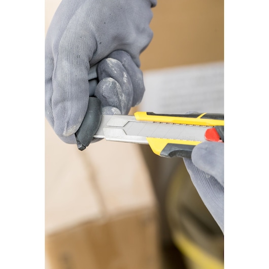 STANLEY FMHT10338-0 utility knife with yellow and black handle, close-up in gloved hand during use.