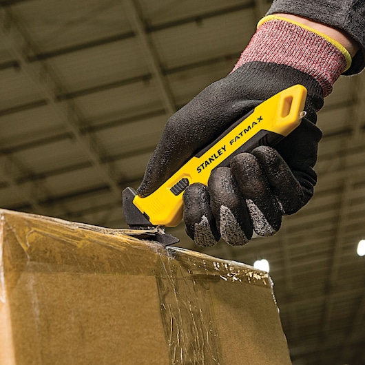 Stanley FMHT10358 utility knife cutting box tape, close-up photo of yellow tool in gloved hand.
