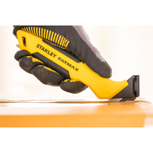 Photo of STANLEY FMHT10373-0 utility knife in a gloved hand, cutting tape on a cardboard box.