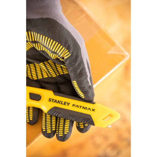 Photo of STANLEY FMHT10373-0 utility knife held by gloved hand, with cardboard box in background.