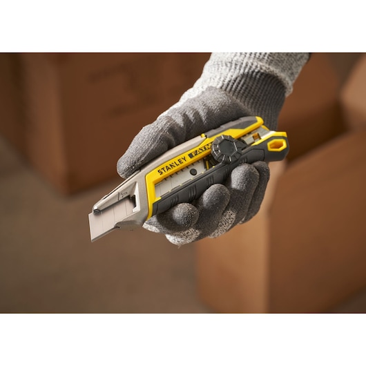 STANLEY FMHT10592-0 utility knife with yellow and gray handle held by gloved hand, photography with cardboard boxes.