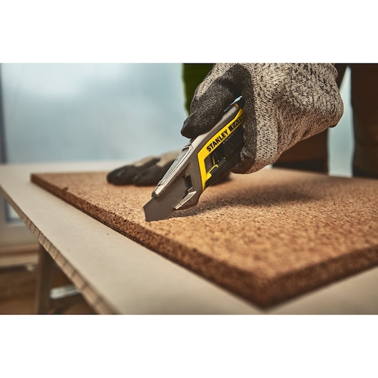 STANLEY FMHT10594-0 utility knife cutting a board, close-up action shot with gloved hand.
