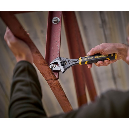Stanley adjustable wrench being used to tighten a bolt on a red metal frame.