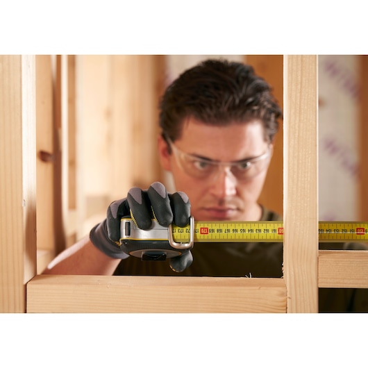 Photo of STANLEY FMHT38232-0 tape measure in use, measuring wooden frame during construction.