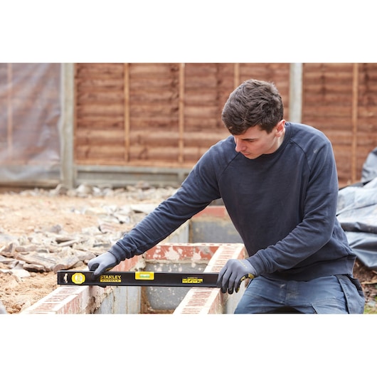 Photo of a person using a STANLEY FMHT42554-1 spirit level on a brick wall at a construction site.