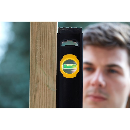 STANLEY FMHT42559-1 photography of black and yellow spirit level held against wooden post outdoors.