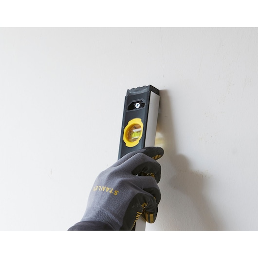 STANLEY FMHT42559-1 spirit level held vertically against a wall by a gloved hand, side angle.