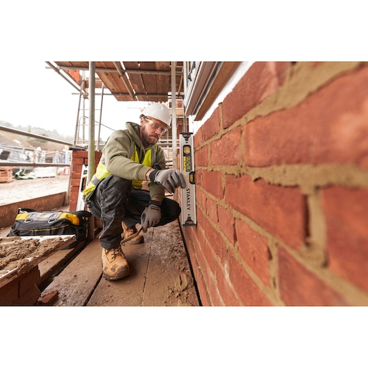 STANLEY FMHT43670-1 spirit level used by construction worker checking vertical alignment of brick wall on site.