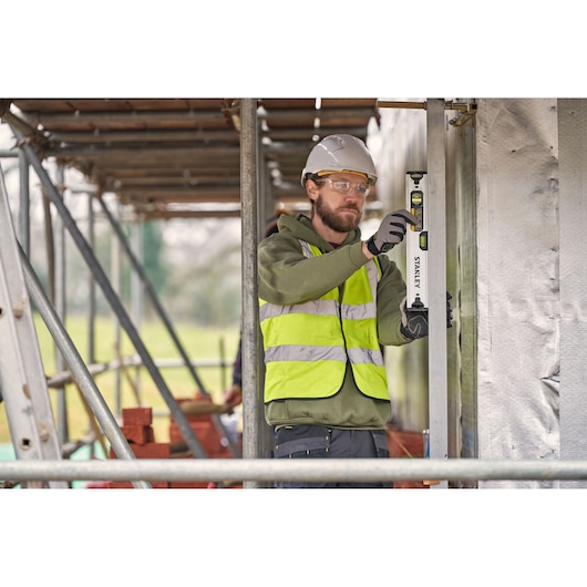 Worker using STANLEY FMHT43670-1 spirit level at construction site wearing safety vest and helmet.