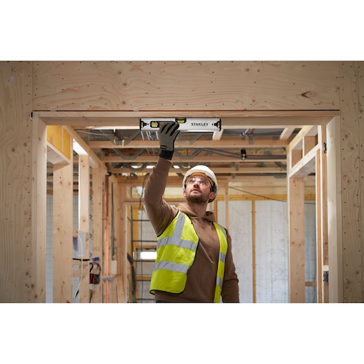 Photo of a worker using a STANLEY FMHT43670-1 spirit level on a wooden door frame at a construction site.