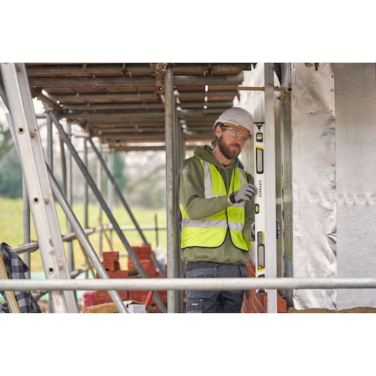 Photo of worker using STANLEY FMHT43674-1 spirit level at construction site, wearing safety vest and helmet.