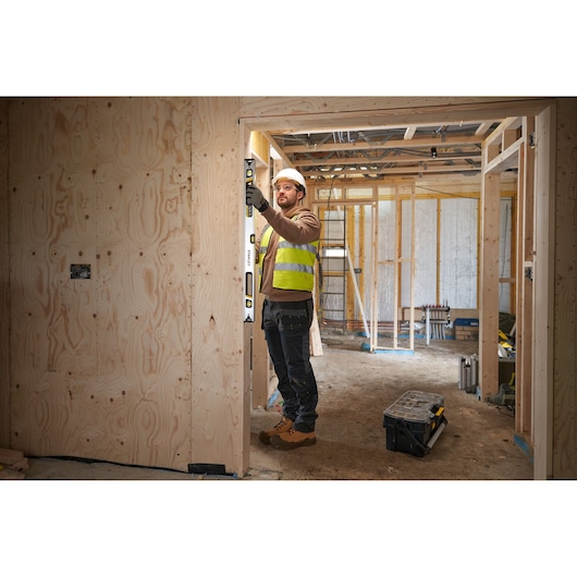 Photo of worker using STANLEY FMHT43674-1 spirit level on wooden door frame at construction site.