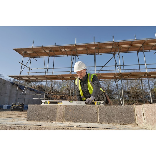 Photo of STANLEY FMHT43675-1 spirit level used on construction site, worker measuring concrete blocks outdoors.