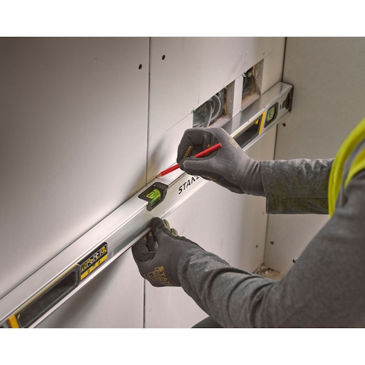 Photo of STANLEY FMHT43675-1 spirit level in use against drywall, worker marking line with pencil.