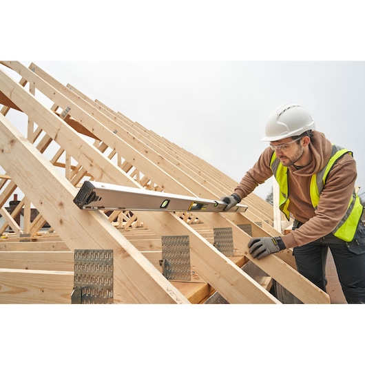 STANLEY FMHT43679-1 spirit level in use on wooden roof trusses by a worker wearing safety gear.
