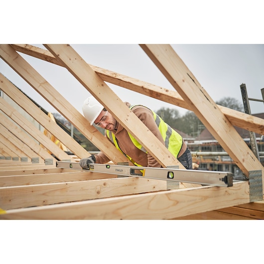 Photo of STANLEY FMHT43679-1 box beam level used by a worker in construction, measuring roof trusses.