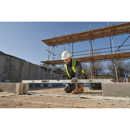 STANLEY FMHT43680-1 spirit level used by a construction worker kneeling at a building site, outdoor setting.