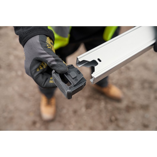 STANLEY FMHT43680-1 tool component held by gloved hand near aluminum track, close-up outdoor view.