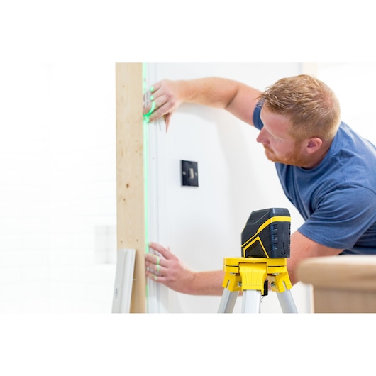 STANLEY FMHT77595-1 laser level on tripod, projecting green line onto wall during installation work.