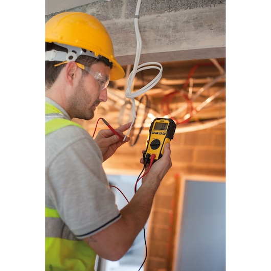 STANLEY FMHT82563-0 digital multimeter used by a worker in a construction setting to test electrical wires.