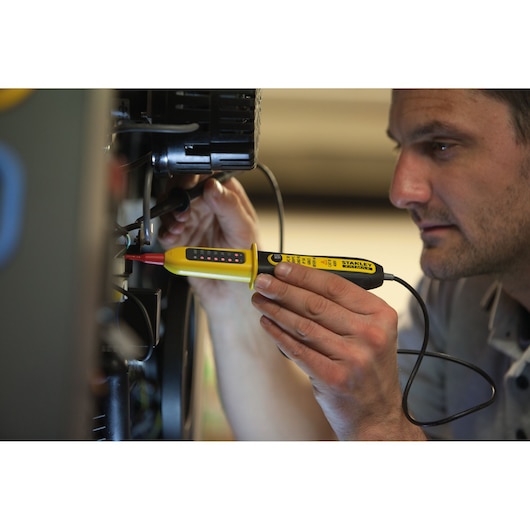 STANLEY FMHT82566-0 voltage tester in use, yellow handheld tool with LED indicators, close-up in electrical setting.