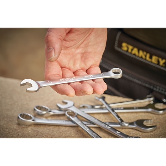 STANLEY FMMT13031-0 combination wrench held in hand, several wrenches on wooden surface, close-up.