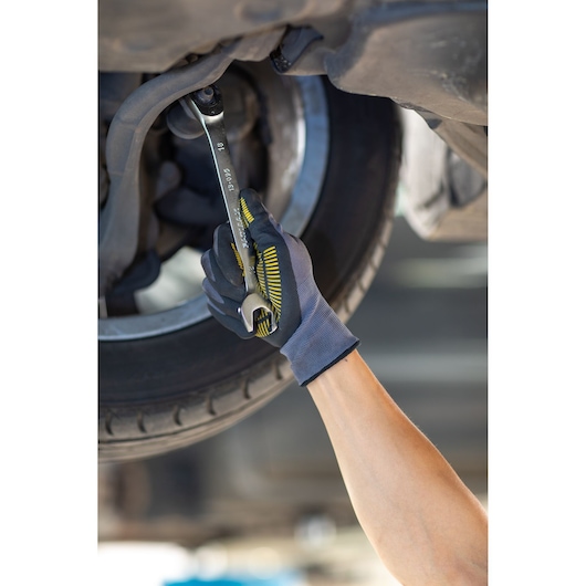 STANLEY FMMT13086-0 wrench held by gloved hand tightening bolt under car wheel, product in use, side angle.