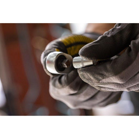 Photo of STANLEY FMMT17207-0 socket wrench in gloved hand, close-up, in a workshop setting.